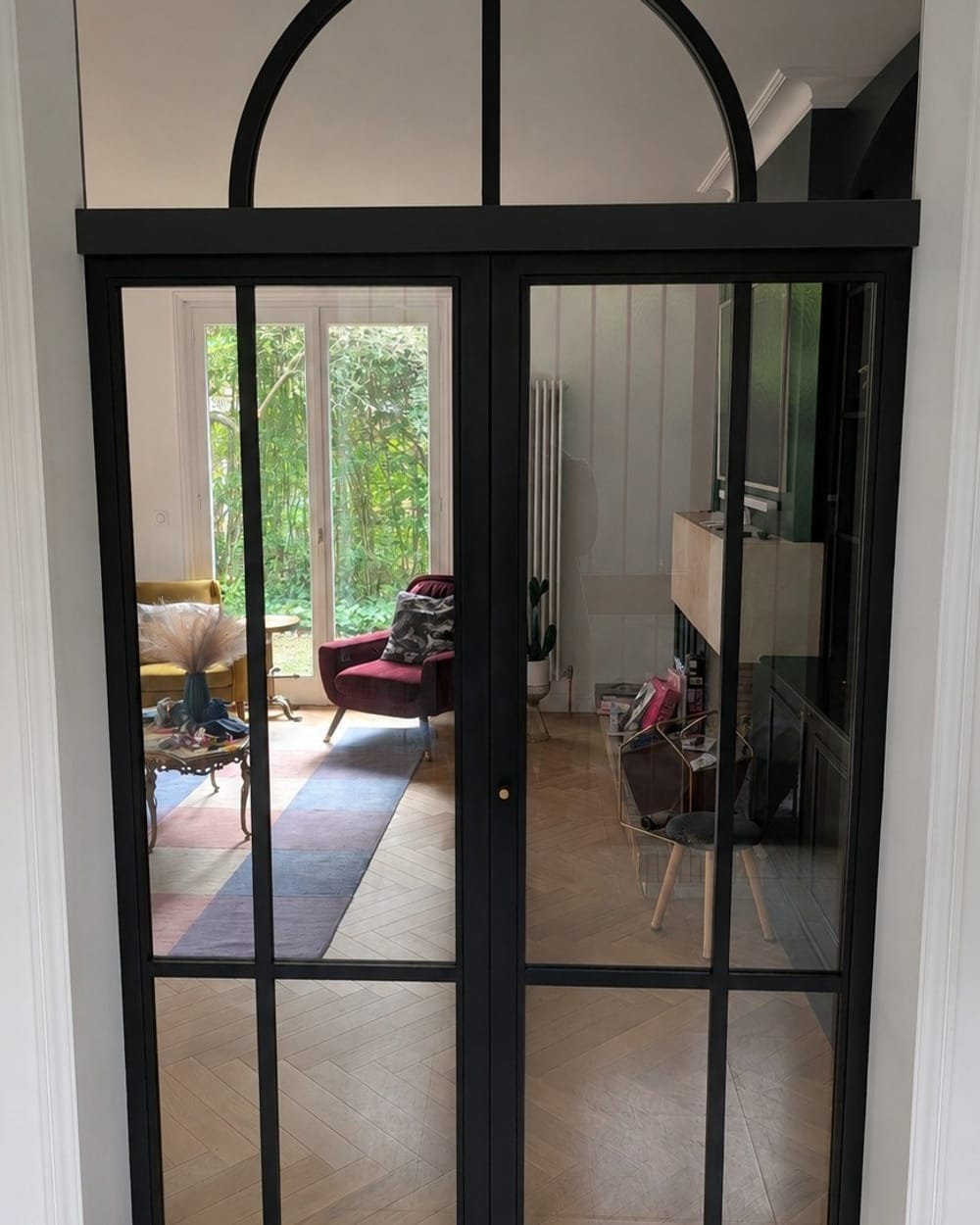 Porte vitrée sur mesure noire à imposte cintrée, ouverte sur le salon